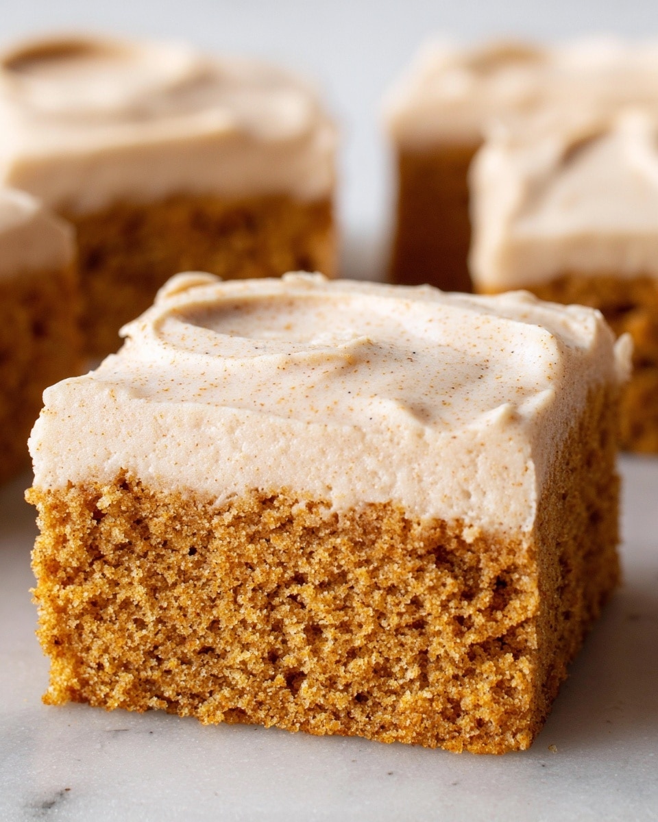 The image shows a close-up of a single rectangular piece of cake with two layers. The bottom layer is a moist, dense cake with a golden brown color and a slightly crumbly texture. The top layer is a thick, creamy frosting in a light beige color, spread evenly with small textured peaks and a light sprinkle of fine brown spices on top. The cake piece sits on a white marbled surface with a soft natural light enhancing the textures. photo taken with an iphone --ar 4:5 --v 7