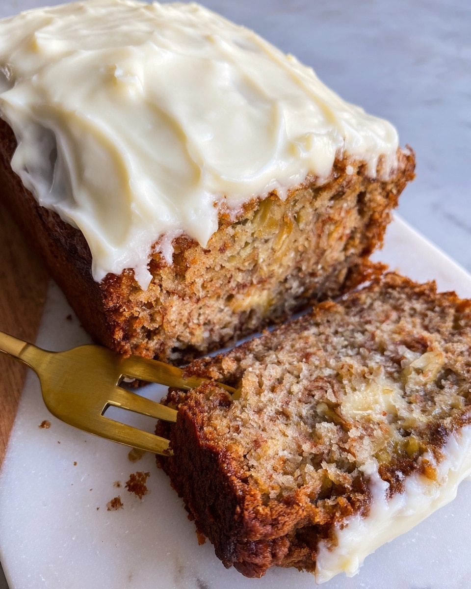 This image shows a thick slice of moist banana bread with a coarse, textured inside that looks dense with visible bits of banana and its brown crust edges slightly crisp. On top, there is a thick layer of creamy white frosting that appears smooth and swirled, covering the whole top of the bread. A gold fork cuts into the front slice revealing its soft inside, while the bread rests on a white plate with a white marbled surface beneath. Photo taken with an iphone --ar 4:5 --v 7