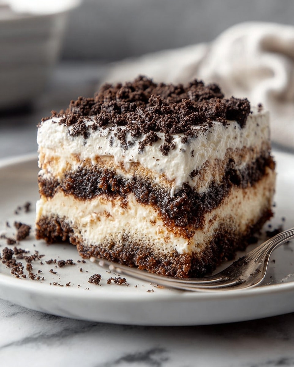 A square piece of layered dessert sits on a white plate with a silver fork beside it. The dessert has three visible layers: a bottom dark brown crumbly layer, a middle creamy off-white layer with bits of darker crumbs mixed in, and a thick top layer of white cream sprinkled generously with dark brown cookie crumbs. The white plate rests on a surface with white marbled texture, and behind it is a blurred background with neutral colors. photo taken with an iphone --ar 4:5 --v 7