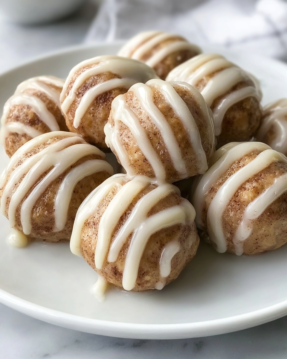 A white plate holds eight small round balls that are light brown with visible cinnamon specks throughout. Each ball is generously coated with a thick, creamy white icing that covers parts of the surface and is drizzled in neat, thick lines over the top and sides. The texture of the balls looks soft but firm, while the icing is smooth and glossy, adding a rich contrast to the slightly grainy cinnamon surface. The white plate sits on a white marbled textured surface, with a soft focus background. photo taken with an iphone --ar 4:5 --v 7