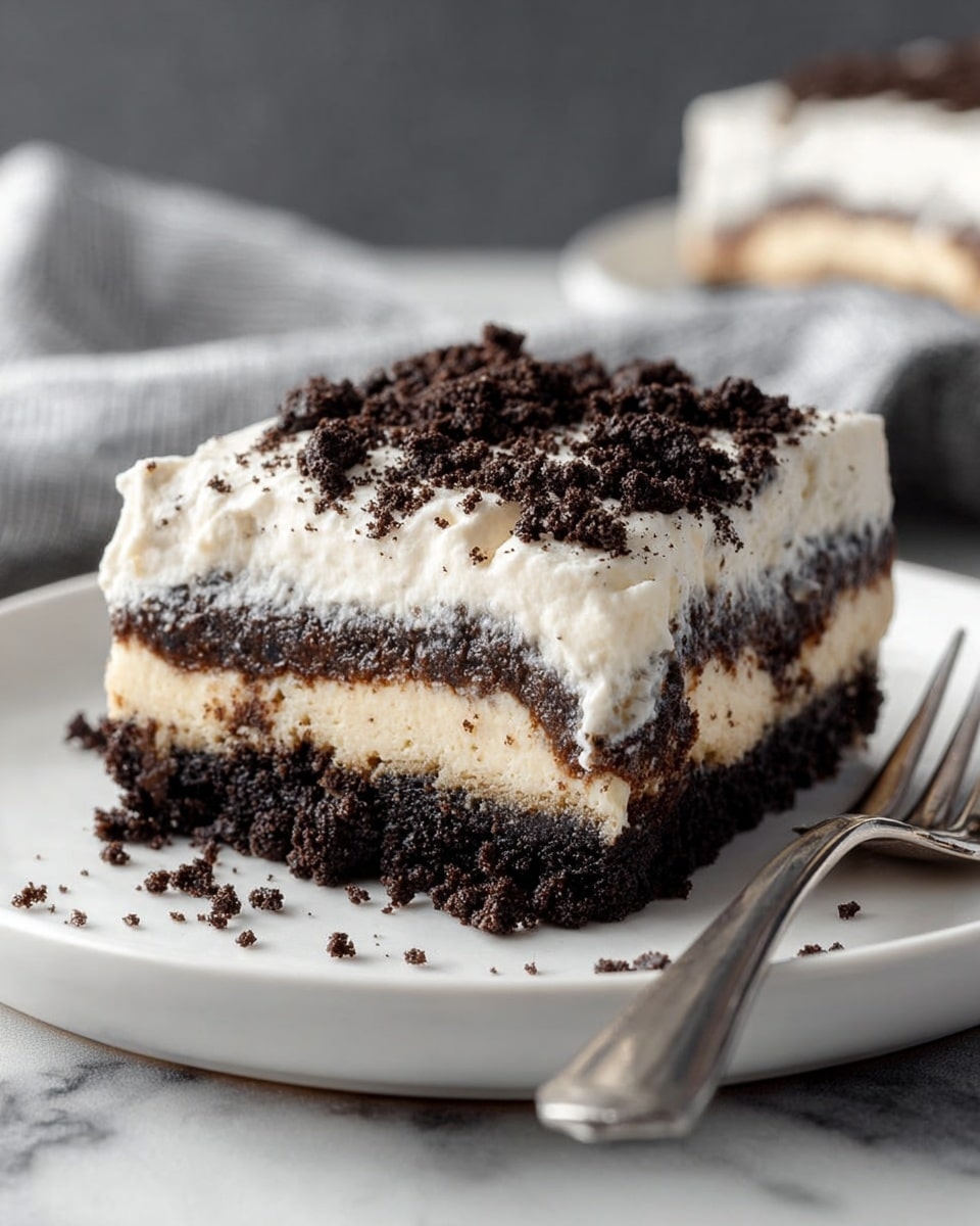 A square piece of layered dessert sits on a white plate, placed on a white marbled surface. The bottom layer is dark brown and crumbly, looking like a rich chocolate base. Above it is a creamy off-white layer that appears smooth and thick. Next is a second dark brown crumbly layer similar to the bottom one. On top, there is a thick layer of white cream with dark chocolate cookie crumbs sprinkled unevenly across it. To the right of the dessert on the plate is a silver fork. The background is softly blurred with gray and white tones. photo taken with an iphone --ar 4:5 --v 7