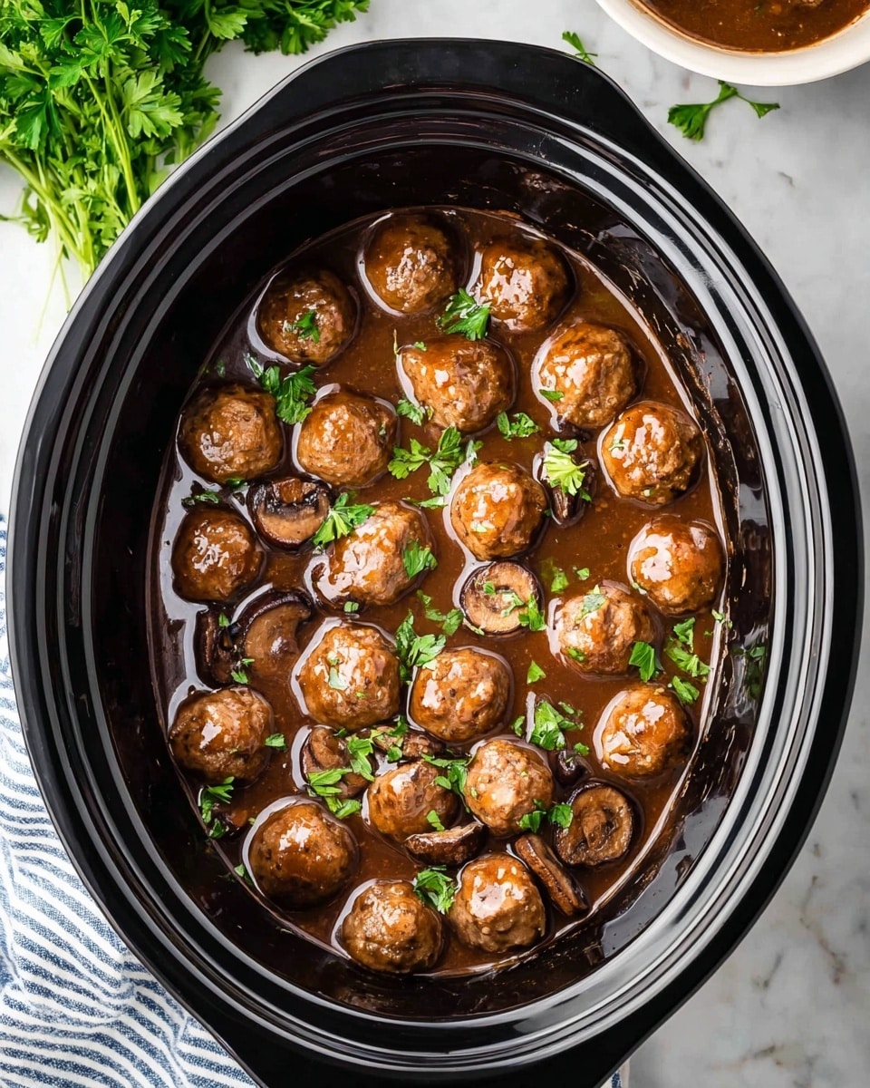A black slow cooker bowl holds a rich brown sauce with roughly 18 round, glossy meatballs evenly spread throughout. Mixed in are several slices of browned mushrooms that add a textured look. The dish is sprinkled with small pieces of bright green parsley, contrasting with the dark sauce and meatballs. The slow cooker sits on a white marbled surface with a small bunch of fresh green parsley in the top left corner, folded cloth with blue stripes at the bottom left visible, and the edge of a white bowl with brown contents in the top right corner. Photo taken with an iphone --ar 4:5 --v 7