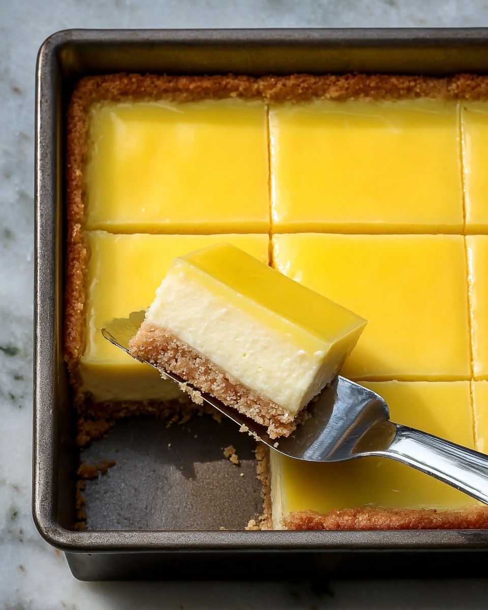 A square lemon bar dessert with three visible layers sits inside a dark metal baking pan on a white marbled textured surface; the bottom layer is a rough, crumbly light brown crust forming the base and edges, the middle layer is a thicker, smooth creamy yellow filling with a dense appearance, and the top layer is a glossy, vibrant yellow lemon custard that looks silky and soft; two lemon bars have been cut into squares from the pan, and a metal spatula is lifting one square to the right side, showing clean edges and the three distinct layers clearly. Photo taken with an iphone --ar 4:5 --v 7